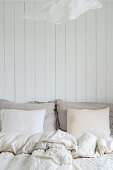 Bed linen in pale shades against board wall