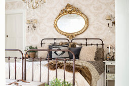 Oval, gilt-framed mirror above vintage metal bed