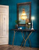 Deep blue hallway with console table on branches as legs and chandelier reflected in mirror