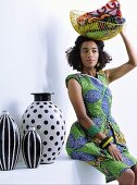 Young woman wearing ethnic dress holding wire basket next to black and white vases