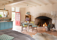 Open fire in large fireplace, kitchen table and double bed in open-plan interior