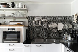 Kitchen utensils hung from rod on ornate, black-and-white, tiled splashback and oven below open shelves