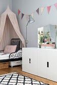 Bed with pink canopy and pastel bunting on wall in girl's bedroom