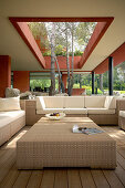 Polyrattan furniture in outdoor lounge on roofed terrace with trees growing through opening in roof
