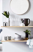 Shelf with dishes and flower vase under a round wall mirror