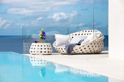 White outdoor furniture next to pool with view of sea and clouds in blue sky