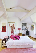 Double bed with white bedspread and hot-pink cushions under wood-beamed ceiling in bedroom