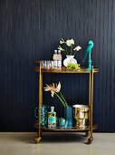 Cocktails, flowers and wine cooler on gilt serving trolley against black-clad wall