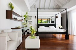 Schwarzes Bettgestell und weiße Bettwäsche in elegantem Schlafzimmer mit Ledermöbeln und Blumenschmuck