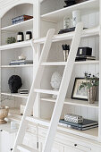 Elegant ornaments on white shelves with library ladder