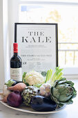 Plate of vegetables, bottle of wine and framed article in front of window