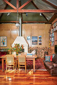 Esstisch mit Stühlen, Vintage Ledersofa und Bücherregal in hohem Wohnraum mit Kamin und Holzlager an Kassettenvertäfelung