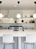 Beleuchtete, weiße Küche mit Küchentheke, Spüle und Barhockern