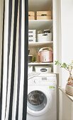 A utility room with washing machine behind a striped curtain