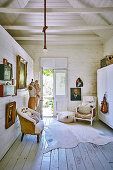 Sessel, Holzschrank, Schneiderpuppen, Goldrahmen-Bilder im Zimmer mit Tür zum Garten