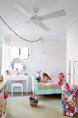 Weisses Kinderzimmer mit bunten Accessoires, Mädchen liegt mit Buch auf Bett