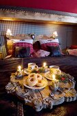 China and lit candles on carved antique wooden tray on bedspread in chalet bedroom
