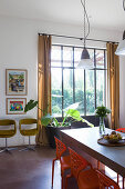 Dining table and orange chairs in front of floor-to-ceiling industrial window