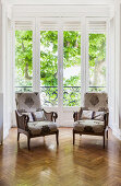 Two armchairs with patterned covers in front of floor-to-ceiling windows