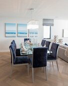 Blau gepolsterte Stühle um Esstisch vor Bilder mit Meer-Motiv in offenem Wohnraum