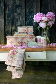 Romantisches Stillleben mit Pfingstrosenstrauß und dekorativen Pappschachteln mit nostalgischem Flair vor rustikaler Bretterwand