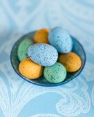 Colourful speckled eggs in bowl on pale blue tablecloth