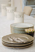 Cutlery and stacked vintage-style plates in front of storage jars on table