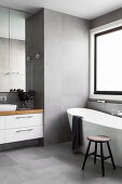 Freestanding bathtub in front of window and vanity in gray tiled bathroom