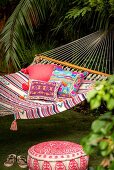 Pouffe below cushions with ethnic patterns in hammock in exotic garen
