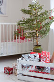 Wrapped presents in white-painted wooden crate in front of small Christmas tree