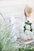 White hydrangeas on old chair with hat hung on board wall