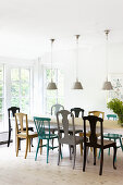 Three ceiling lamps above dining table and various brightly coloured chairs