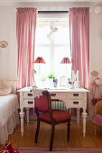 Red upholstered chair and antique desk below window in child's bedroom