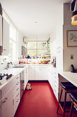 White base cabinets and breakfast bar in narrow kitchen with red floor