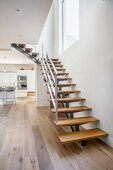Modern staircase with wooden treads in modern interior with kitchen in background