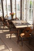 Old wooden tables and chairs with turned legs on rustic board floor next to glass wall