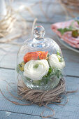 Glass bowl with ranunculus flowers in wreath of grass