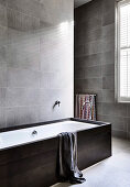 Bathtub in the bathroom with gray-tiled wall tiles