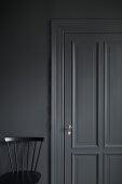 Black chair against grey wall with grey panelled door