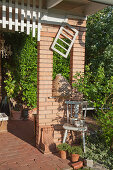 Brick pillar with aperture and rustic arrangement of potted plants and chair on terrace