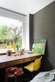 Schreibtisch mit Katze vor Fenster, Drehhocker und gelber Schalenstuhl