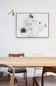 Various wooden chairs around simple dining table below artwork on wall