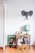 Globe on child's table with cantilever chair below felt elephant head on white wall in child's bedroom