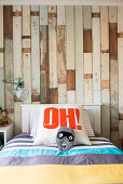 Bed with letter pillow in front of wallpaper with wooden motif