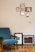 Sessel mit blauem Bezug neben gerahmten Fotos und Wandspiegeln
