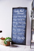 DIY chalk board with weekly menu leaning against the wall, basket with vegetables in front of it