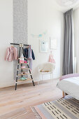 Clothes rack and chair in girl's bedroom with pale grey accents
