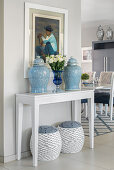 Symmetrical arrangement of lidded jars on console table with matching stools below