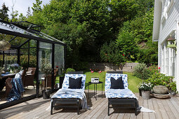 Two loungers on sunny wooden deck between conservatory and house