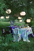 Gedeckter Tisch und farblich passender Stuhl unter beleuchteten Laternen im Garten